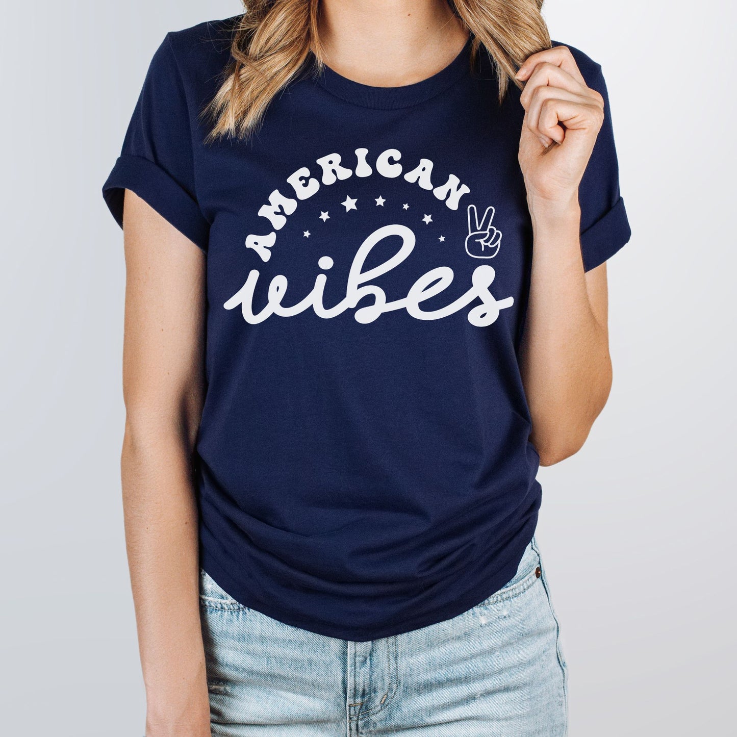 Close-up of woman in navy blue "American Vibes" T-shirt with white stars and peace sign design, rolled sleeves.