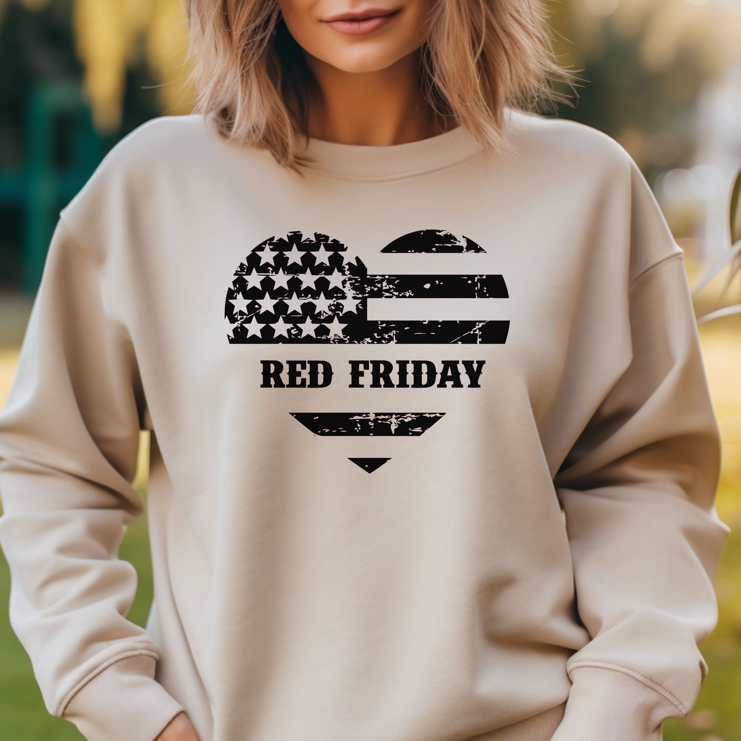 Red Friday heart and flag design on sand-colored women's crewneck, modeled outdoors with natural lighting.