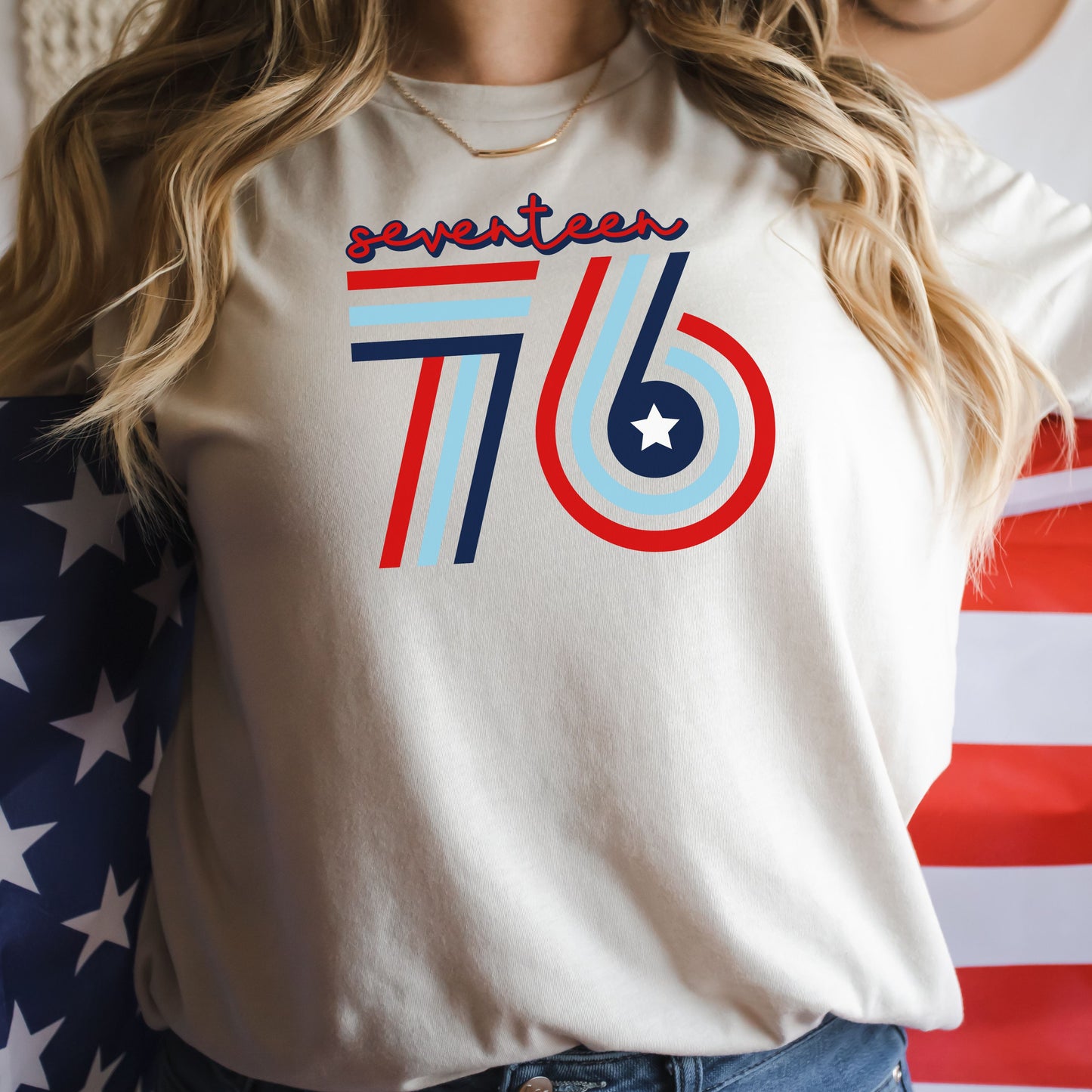 Retro Seventeen 76 in red, white, and blue on natural women's t-shirt, modeled with flag.