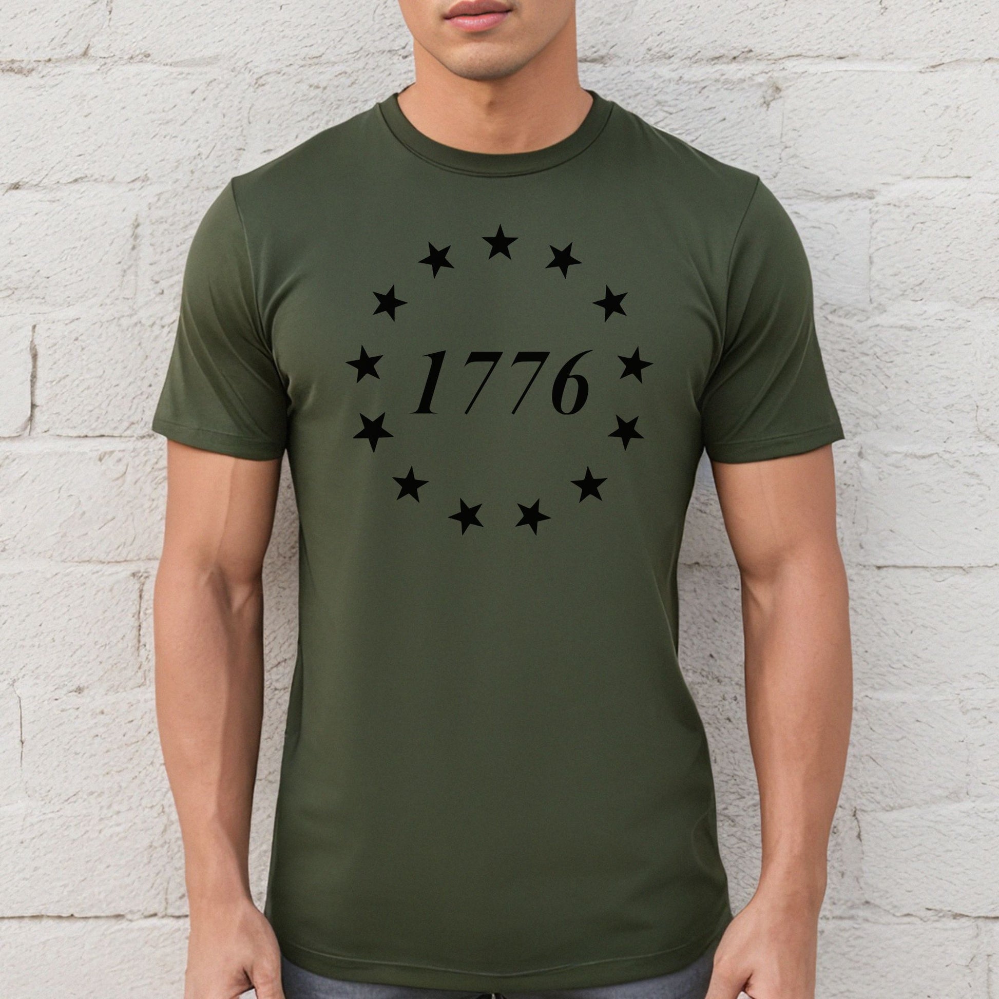 Military green performance tee with black 1776 stars and flag print, worn against a white brick wall.