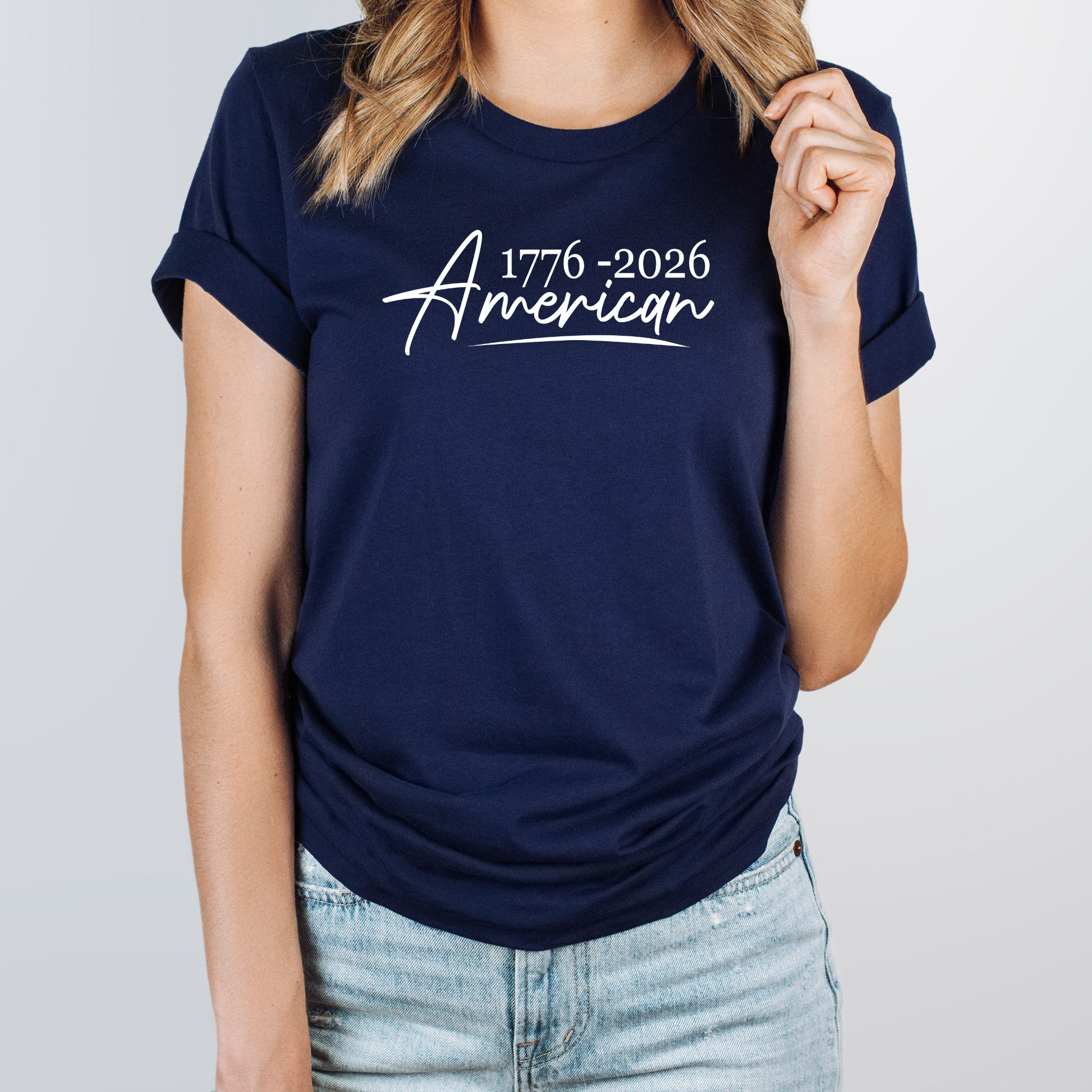Navy blue t-shirt with '1776-2026 American' text worn by a person on a light gray background