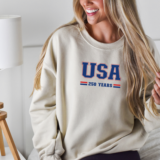 Person wearing a beige sweatshirt with 'USA 250 YEARS' text, sitting indoors.