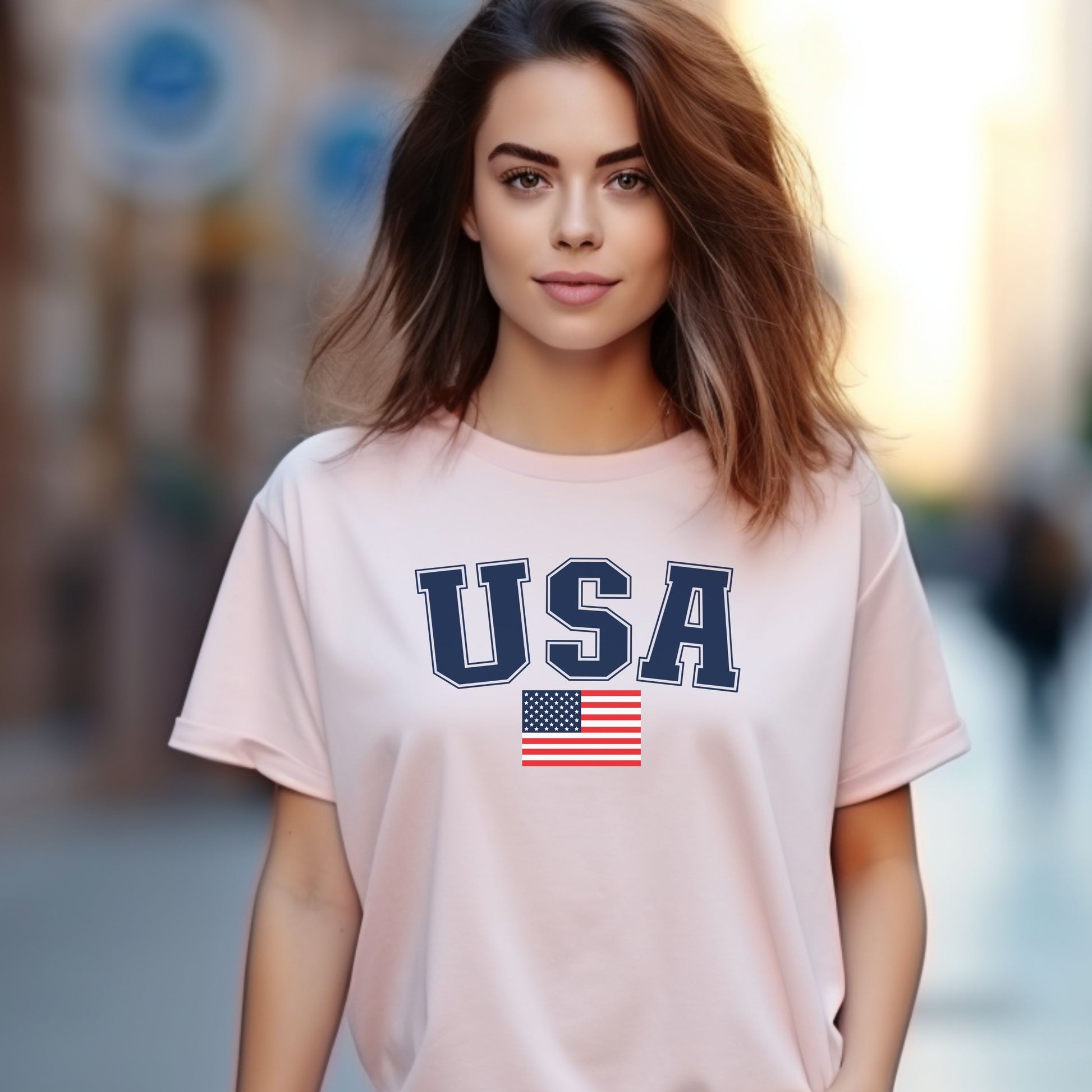 Woman wearing a soft pink patriotic USA t-shirt featuring bold navy USA text and an American flag, perfect for casual patriotic style.