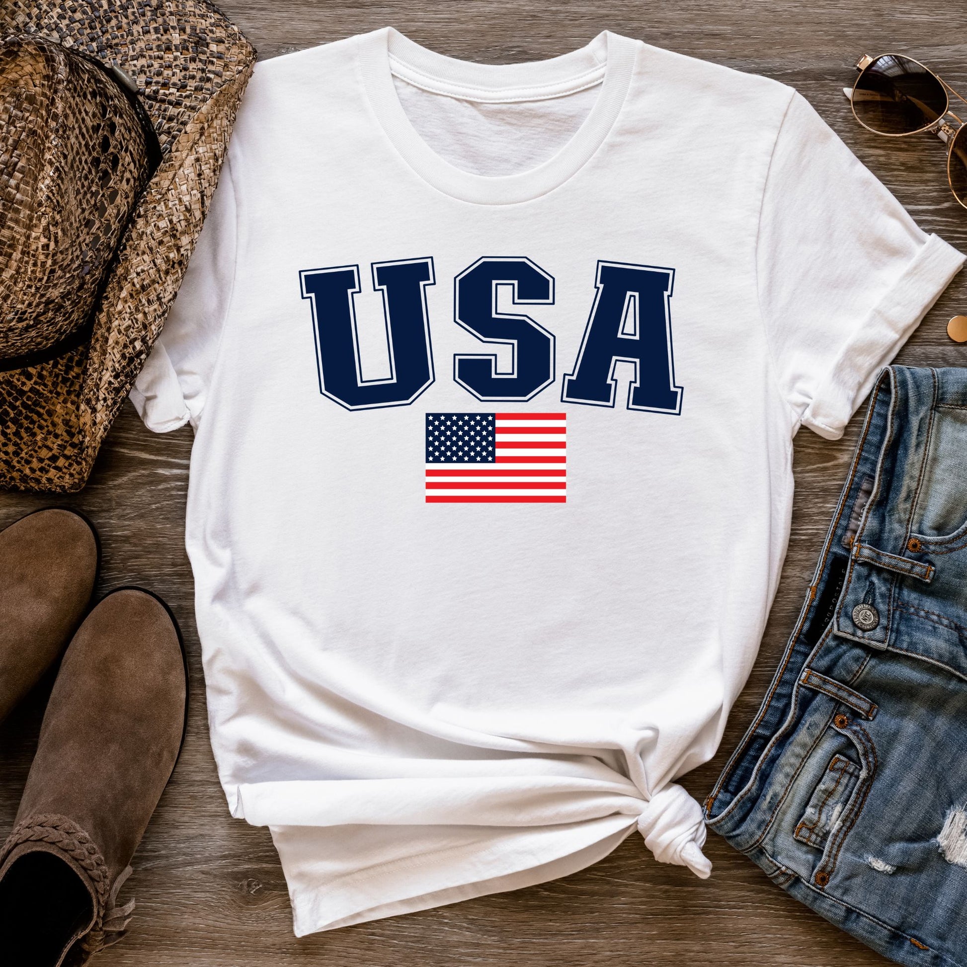 Flat lay of a white patriotic USA t-shirt with accessories, styled for summer festivities like Fourth of July or Memorial Day.