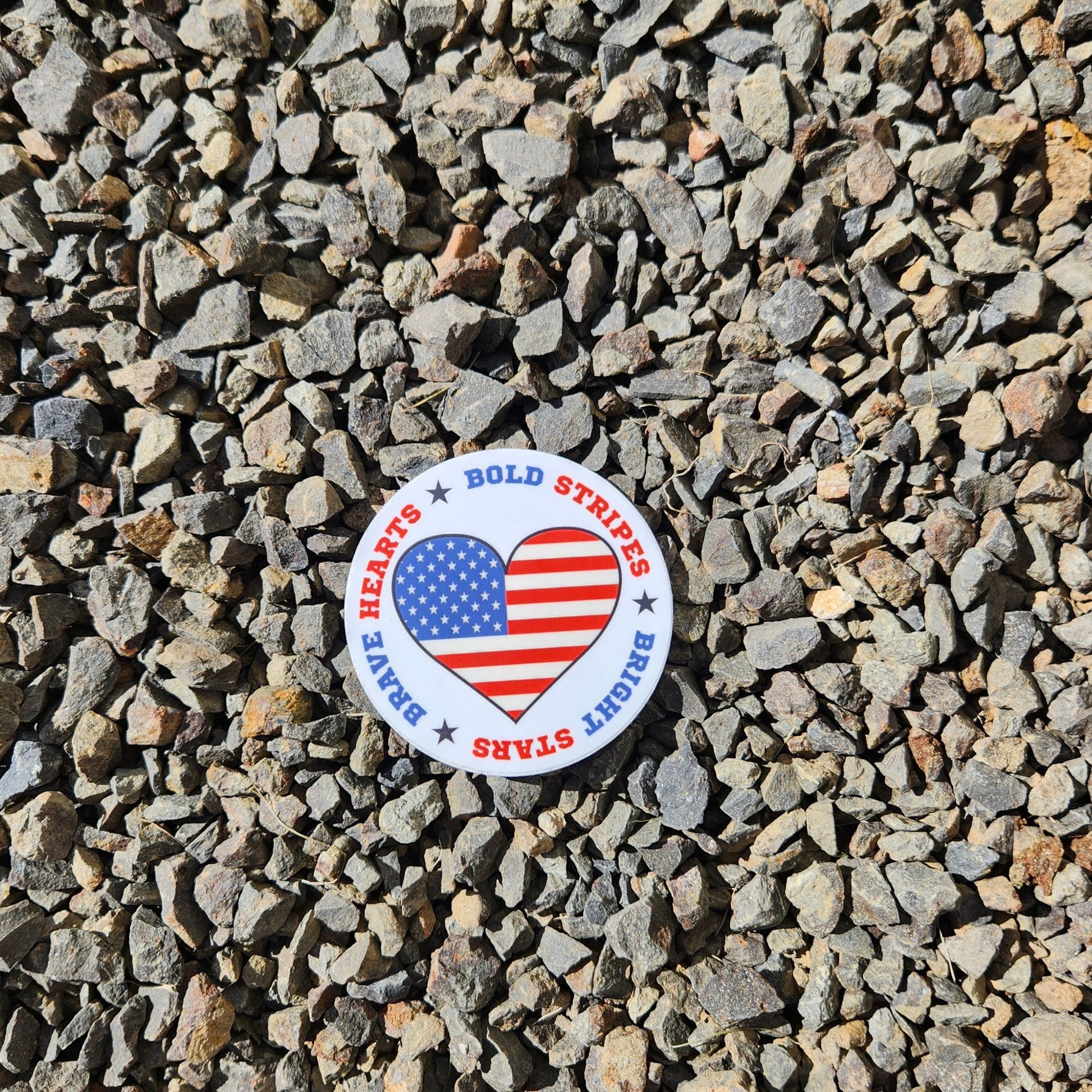 USA heart sticker on rocky gravel background with red, white, and blue patriotic border text.