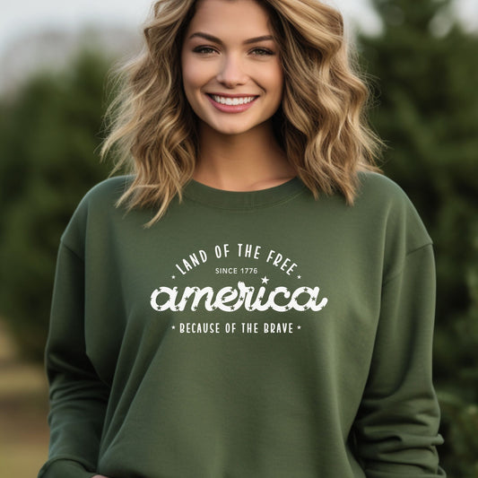 Woman smiling in a military green crewneck that reads "Land of the Free, America, Because of the Brave.