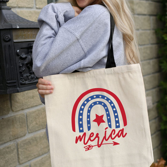 Woman holding patriotic 'Merica canvas tote bag with red, white, and blue rainbow design, shown outside near a black mailbox.