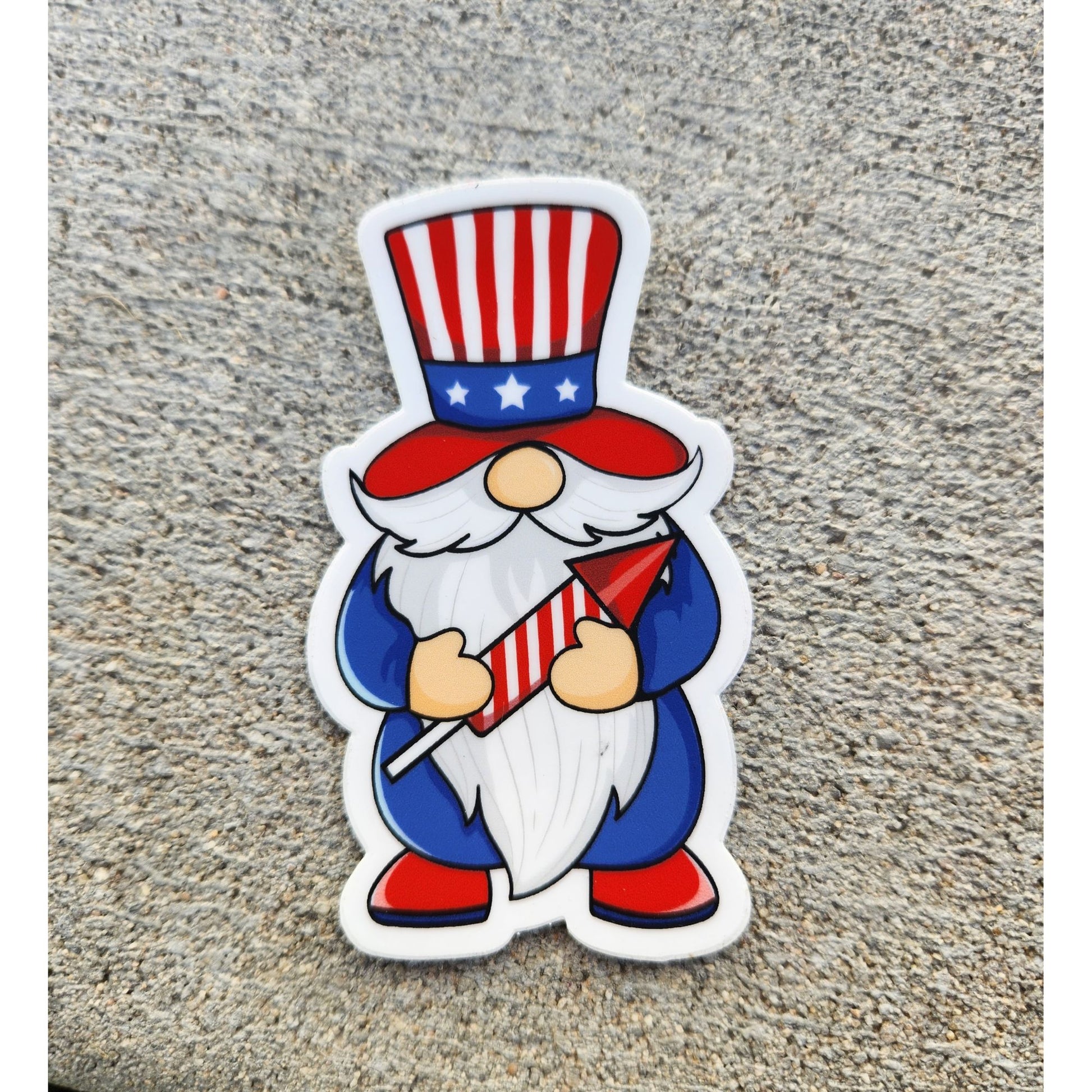 Close-up of a patriotic gnome sticker on concrete, dressed in stars and stripes and holding a firework.