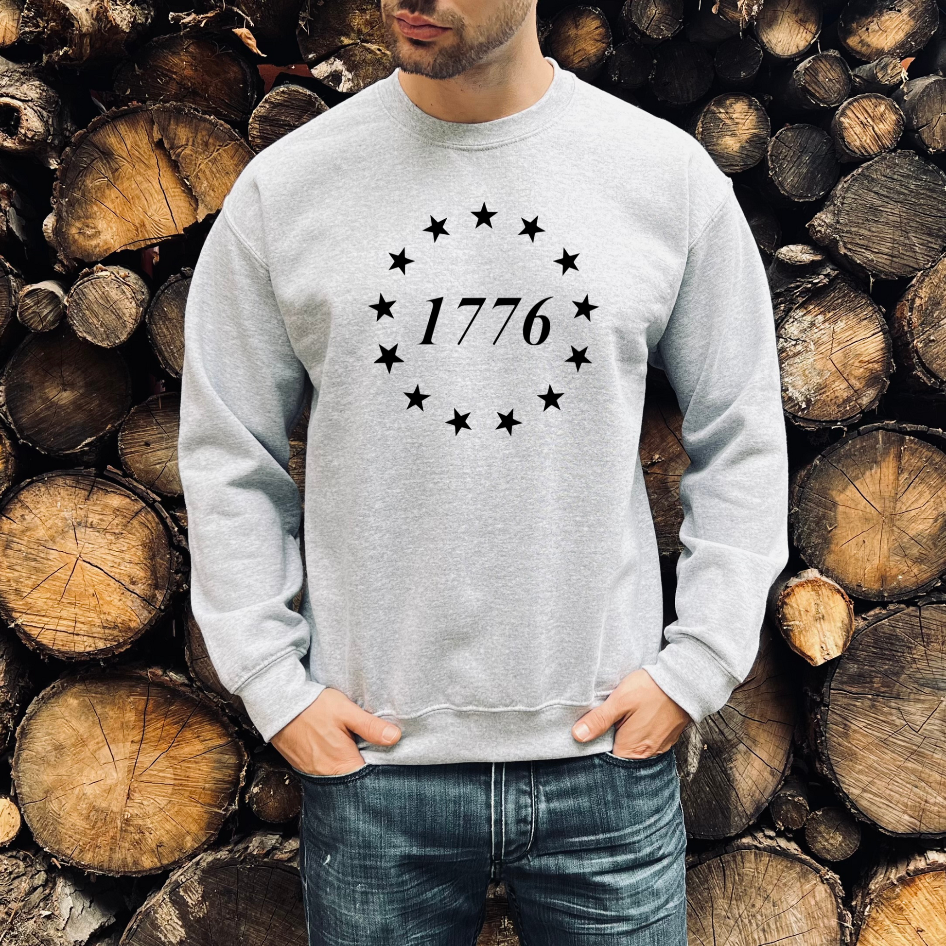 1776 with 13 stars circle on athletic grey crewneck sweatshirt, modeled in front of woodpile.