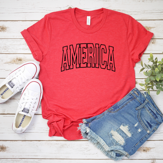 America block lettering on heather red cotton t-shirt, flat lay with sneakers and denim shorts.