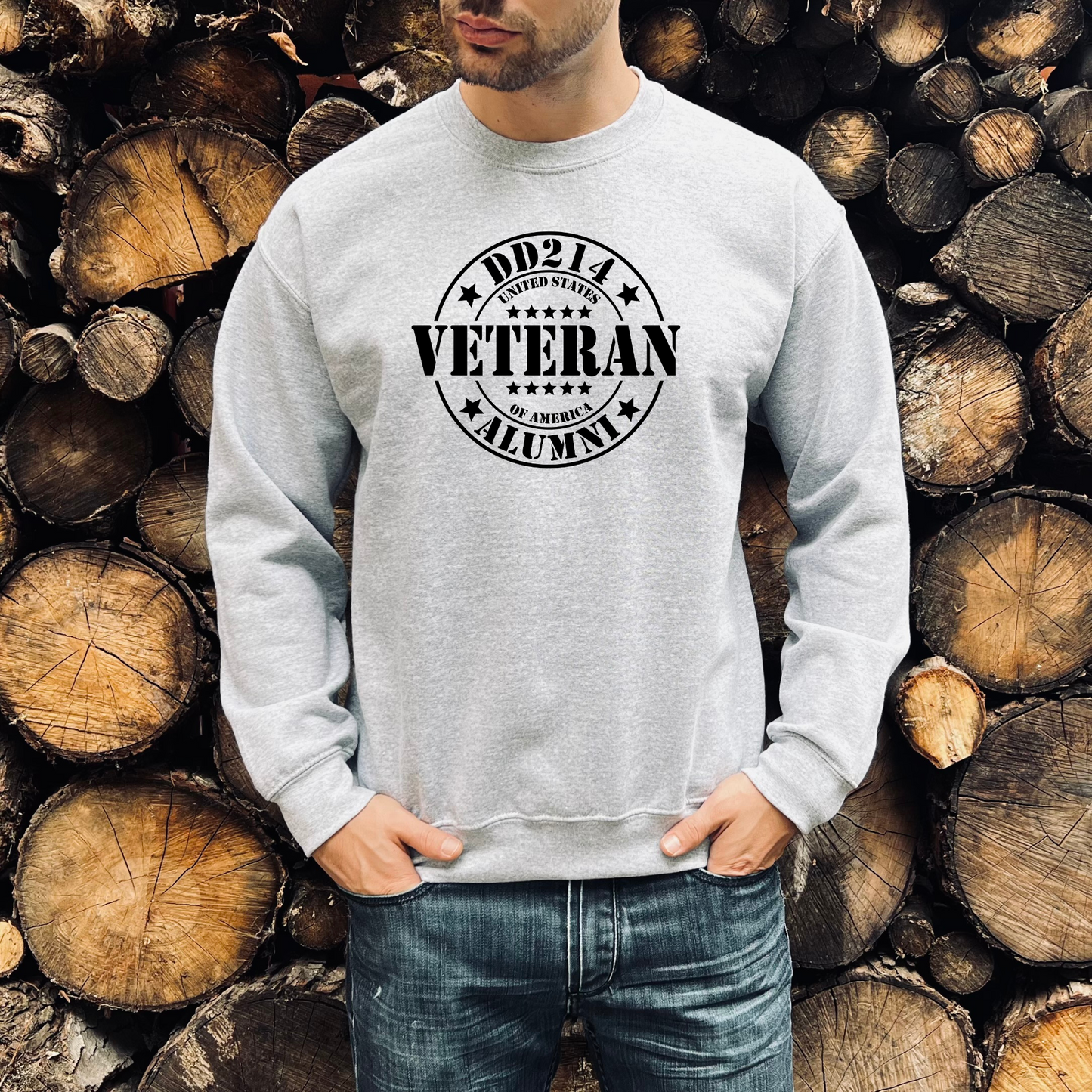 DD214 Veteran Alumni graphic on athletic grey crewneck sweatshirt, modeled in front of stacked woodpile.