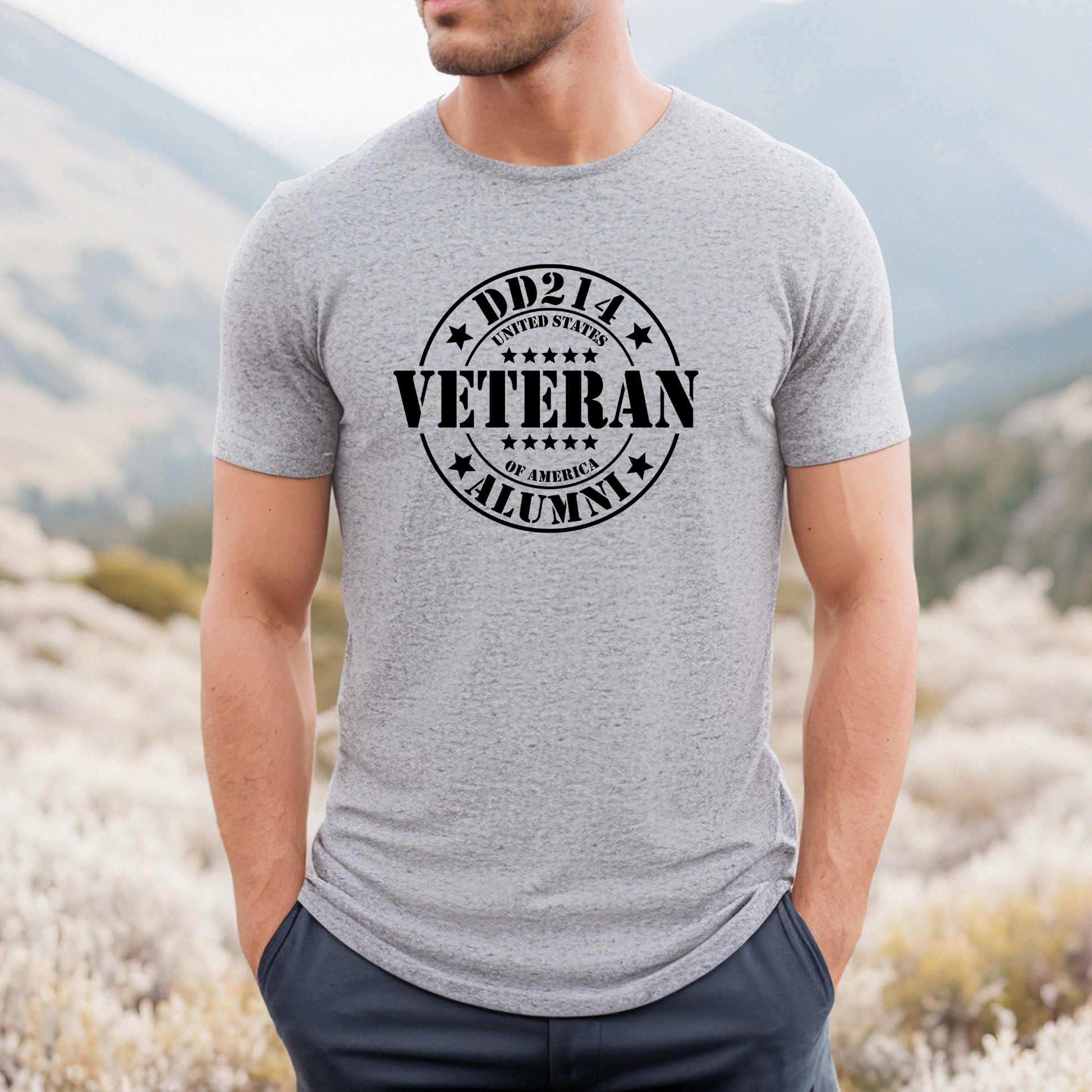 Veteran Alumni circular logo on athletic grey men's t-shirt, modeled in mountain setting.