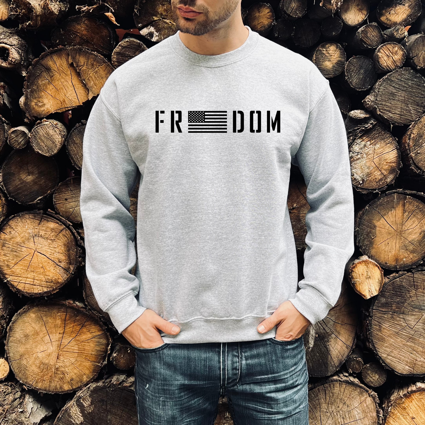 Freedom flag graphic on athletic grey unisex crewneck sweatshirt, modeled in front of woodpile.