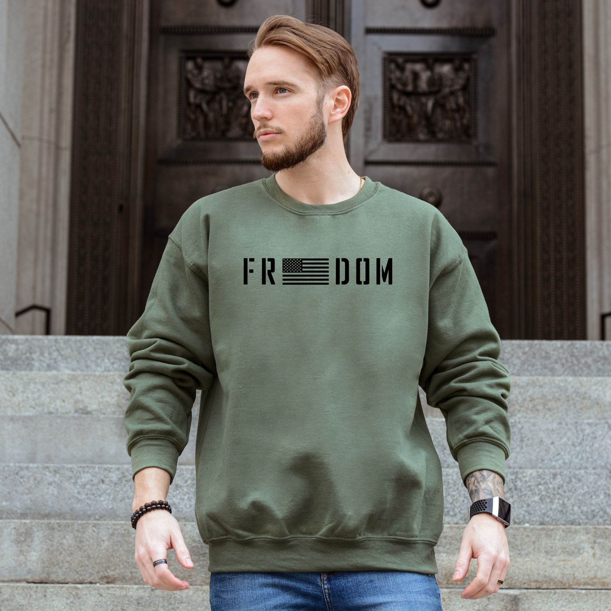 Freedom flag graphic on military green unisex crewneck sweatshirt, modeled on steps.