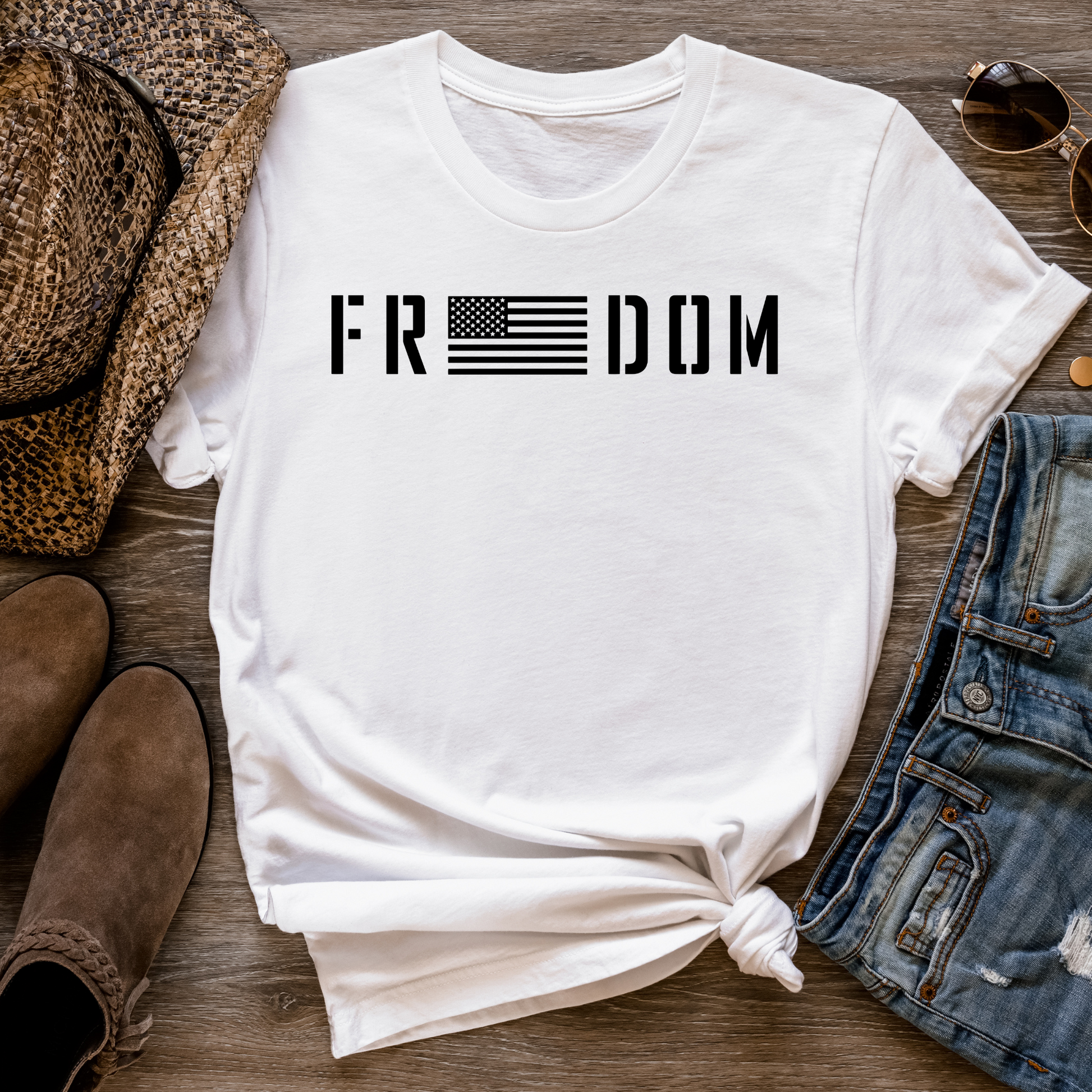 Freedom flag design on soft white cotton unisex t-shirt, flat lay with western accessories. 