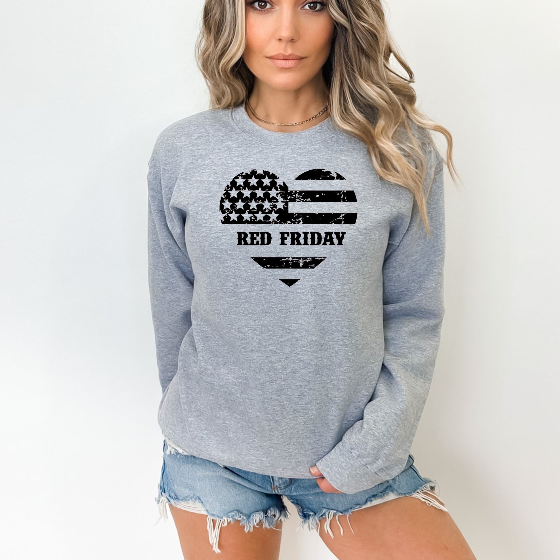 Distressed flag heart with 'Red Friday' on sport grey women's crewneck sweatshirt, modeled with denim shorts.