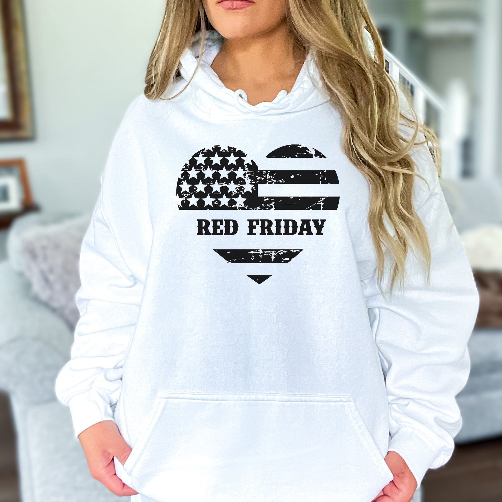 Distressed Red Friday heart flag design on white hoodie, modeled in casual living room setting.