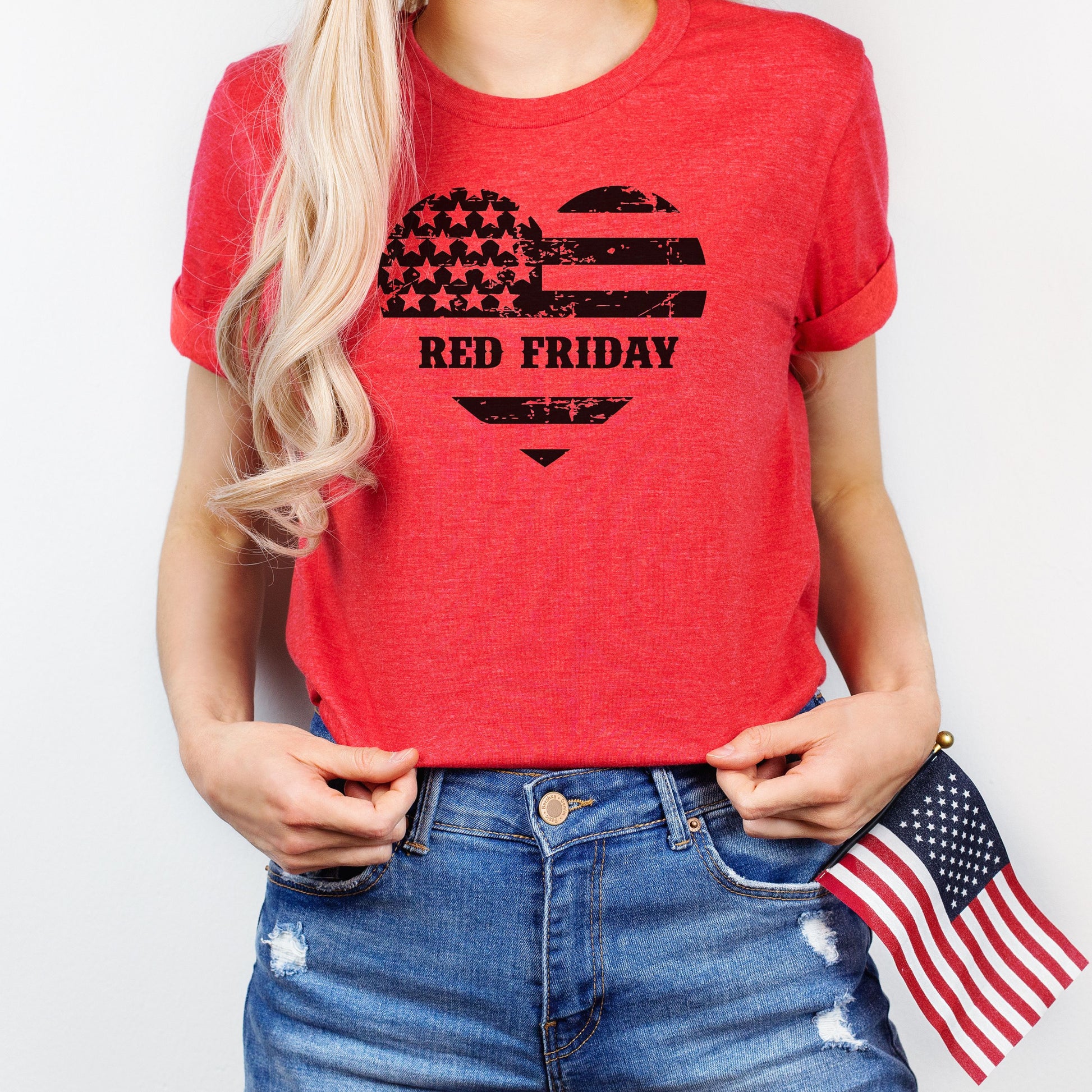 Red Friday heart-shaped flag graphic on soft heather red women's t-shirt, modeled with mini flag.