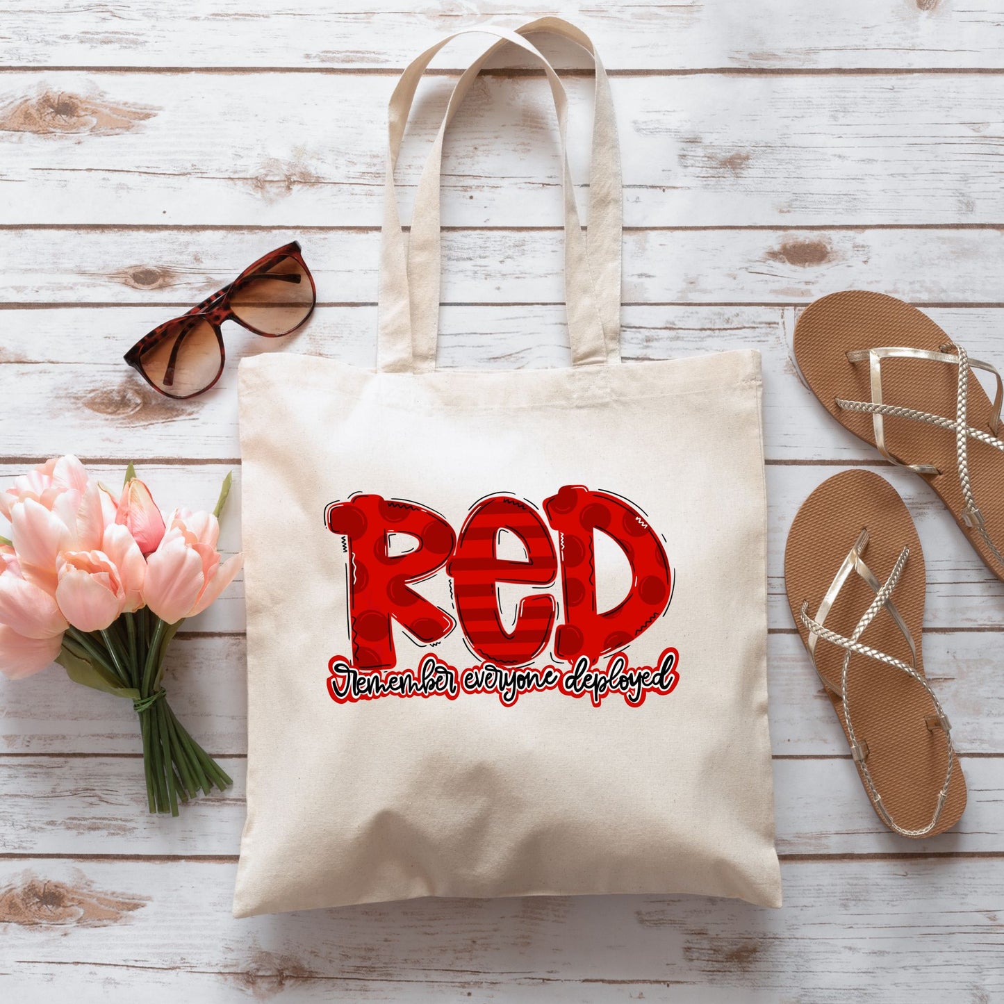 Flatlay of patriotic “RED” tote bag with Remember Everyone Deployed design, surrounded by spring accessories and tulips.