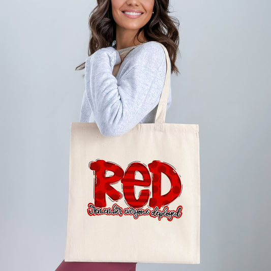 Woman holding patriotic tote bag with bold red “RED” text and “Remember Everyone Deployed” message in script, perfect for showing military support.