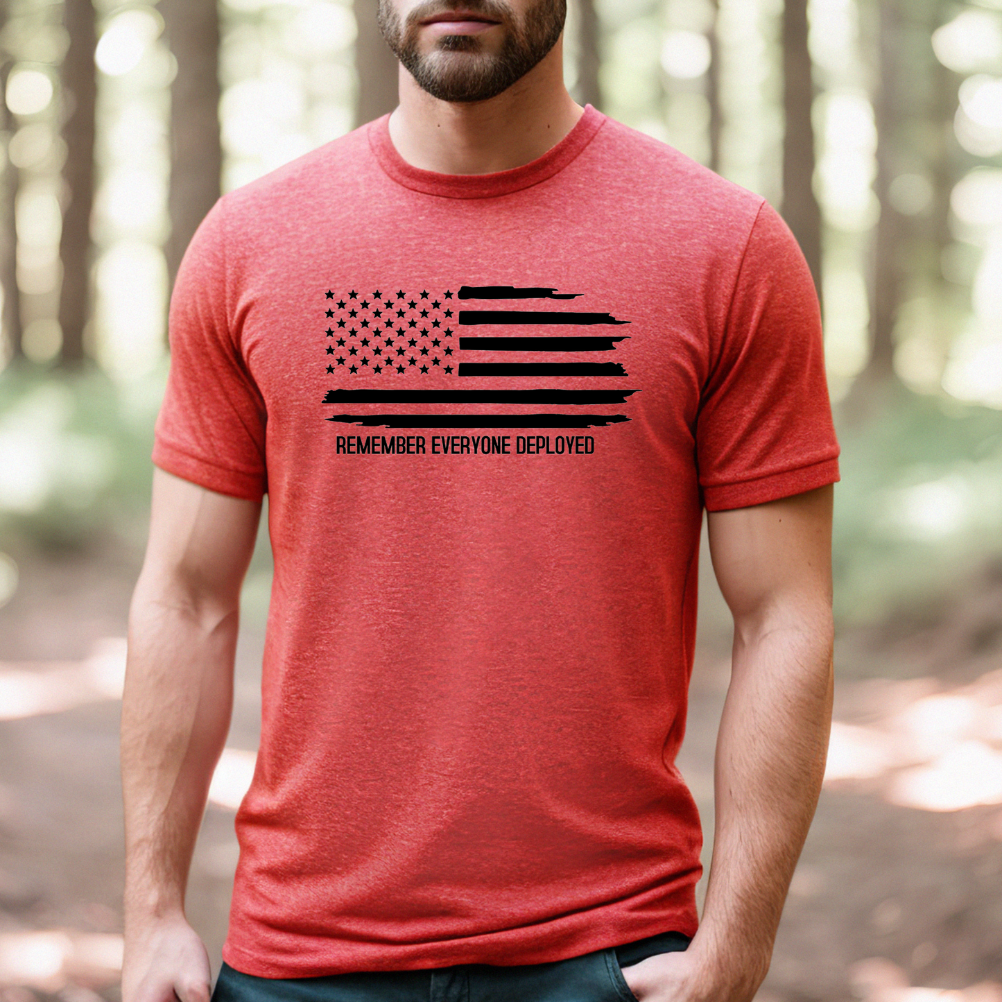 Remember Everyone Deployed flag graphic on heather red men's t-shirt, modeled outdoors in wooded area.