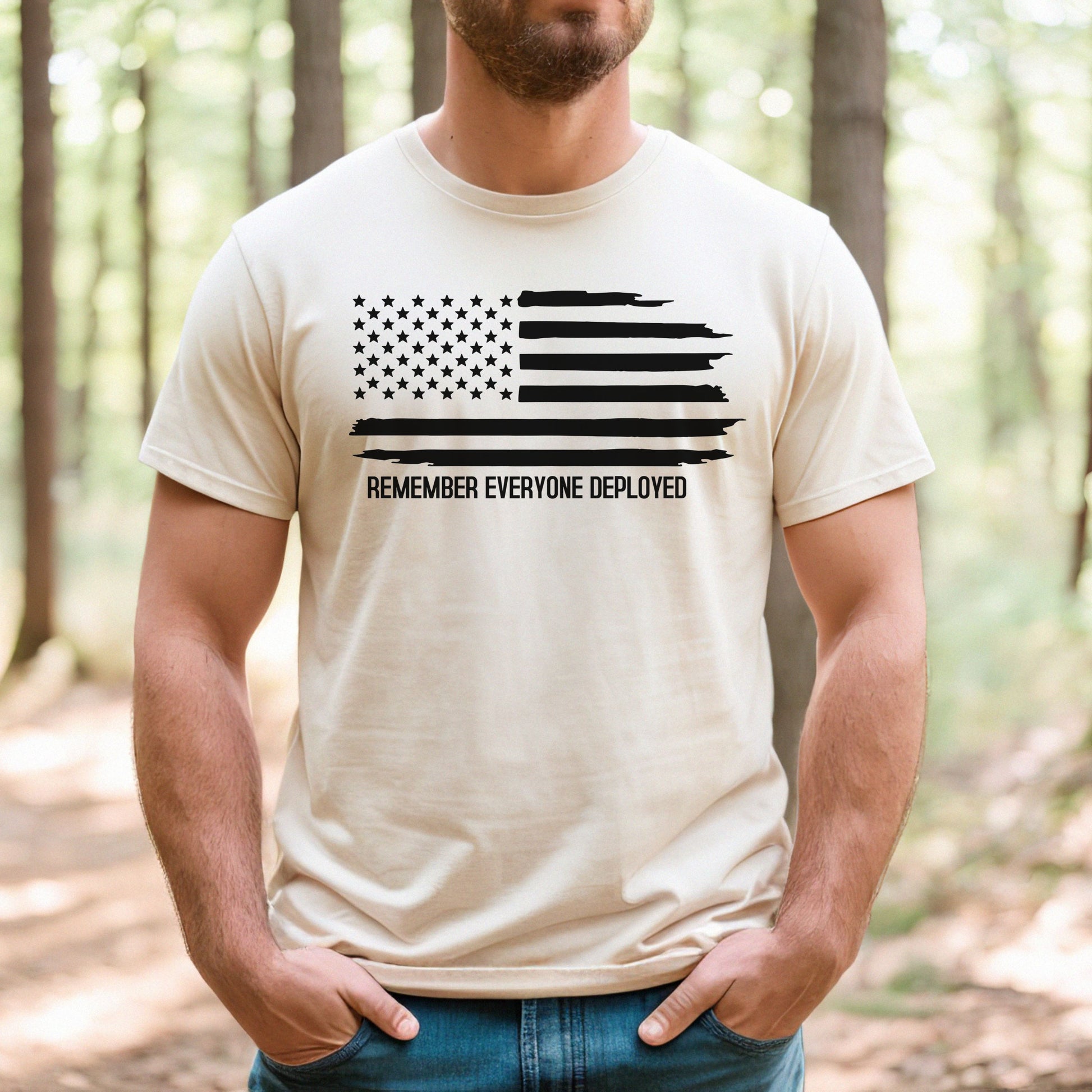 Faded flag and Remember Everyone Deployed text on natural men's t-shirt, modeled in sunlit forest.