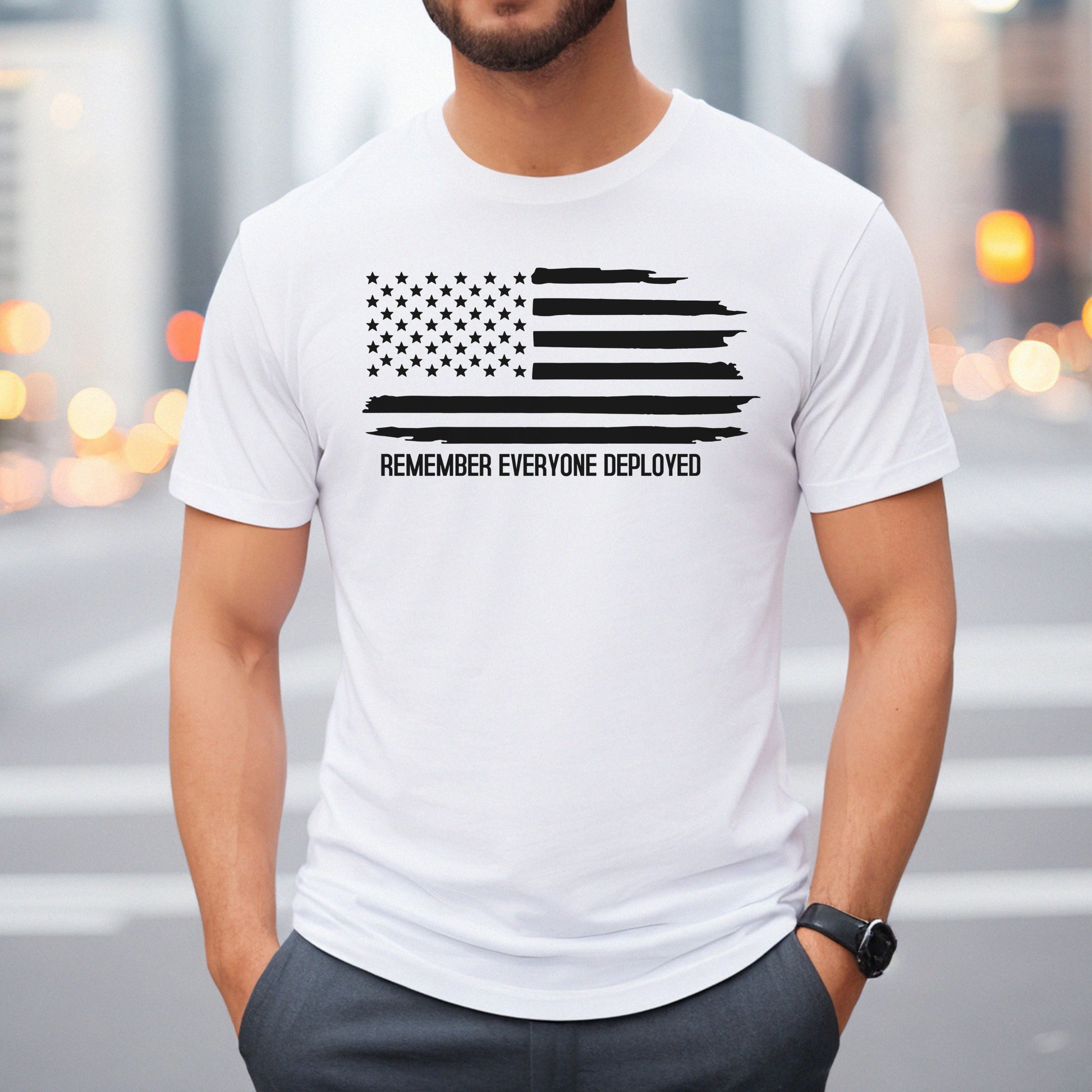 Distressed black American flag with 'Remember Everyone Deployed' on white men's t-shirt, modeled downtown.