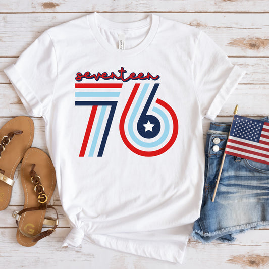 Bold Seventeen 76 design on white t-shirt, flat lay styled with denim shorts, sandals, and mini flag.