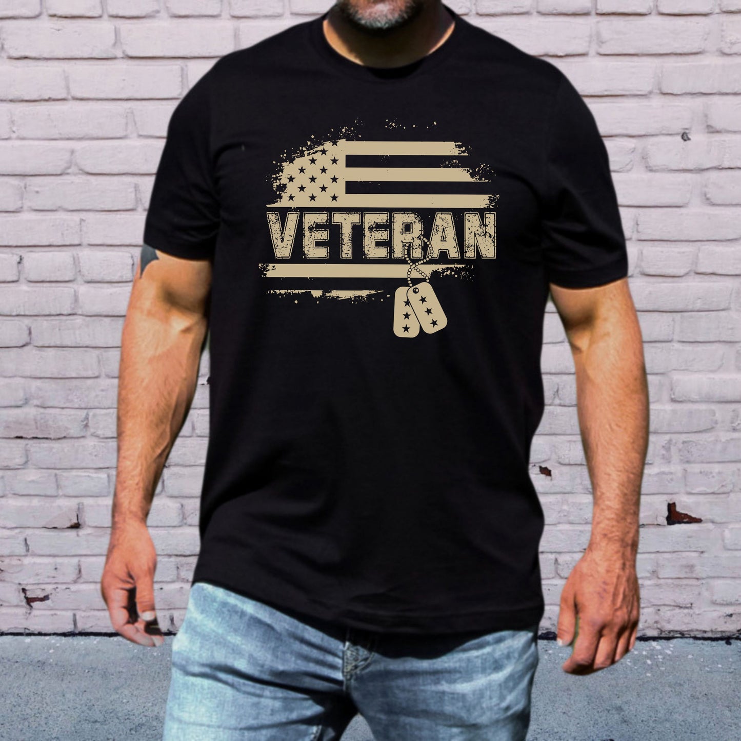 Bold Veteran dog tag flag design on black men's t-shirt, modeled in front of white brick wall.