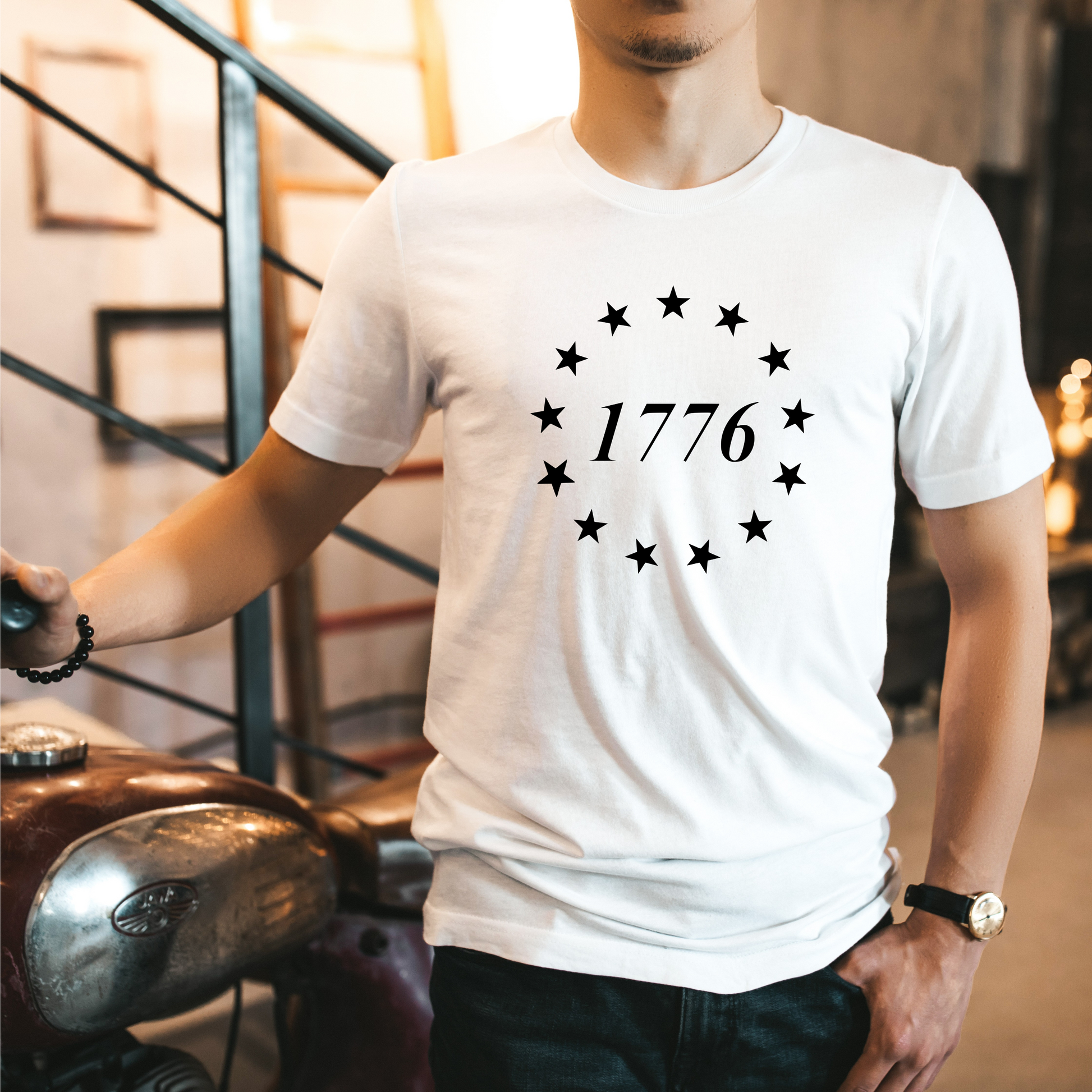 White t-shirt featuring a minimalist 1776 design with 13 black stars in a circular formation.